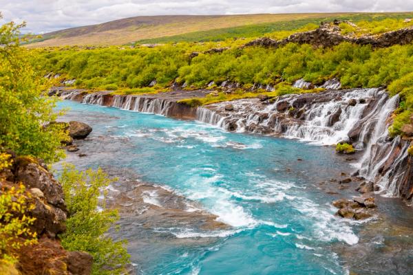 there is a waterfall in the middle of a river surrounded by trees at hraunfossar in iceland.