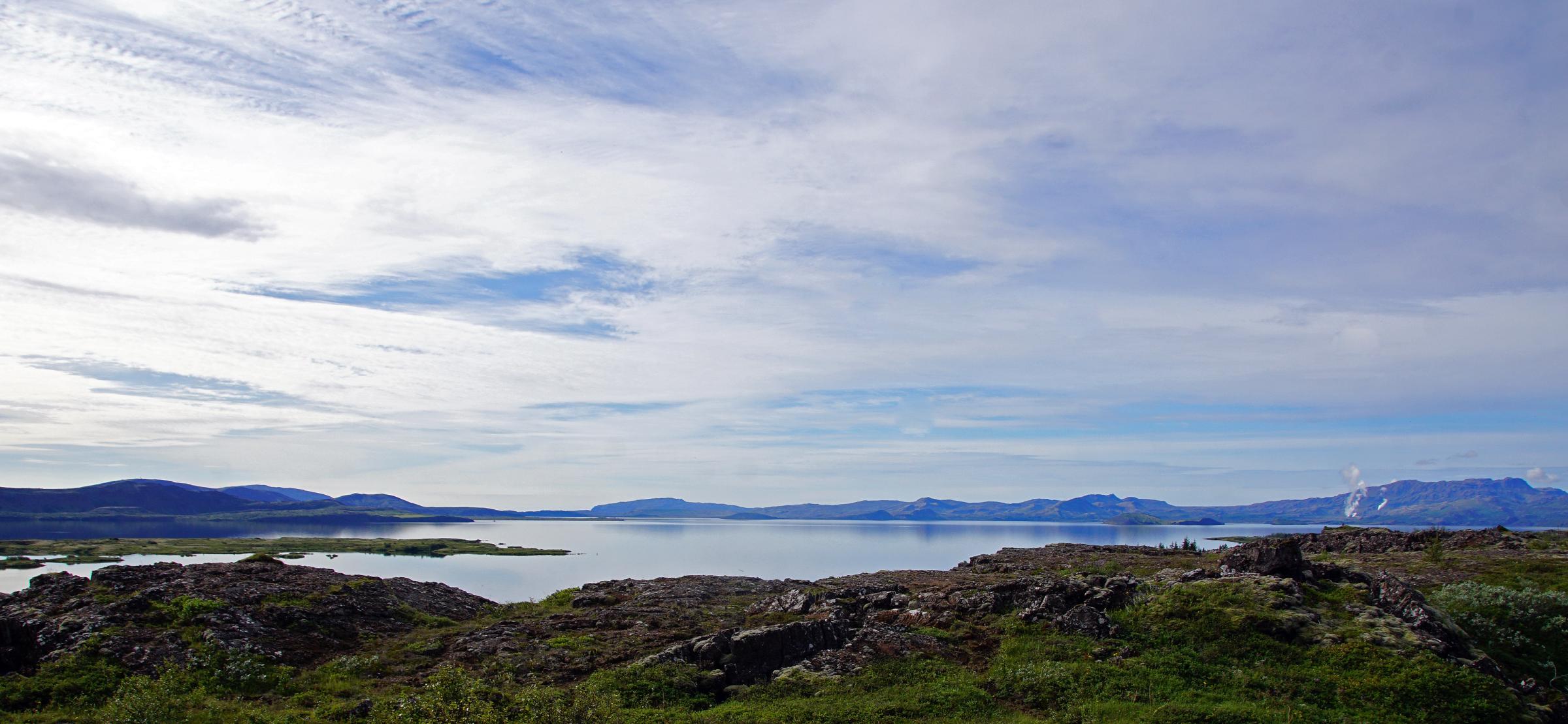 a large body of water surrounded by mountains on a cloudy day .