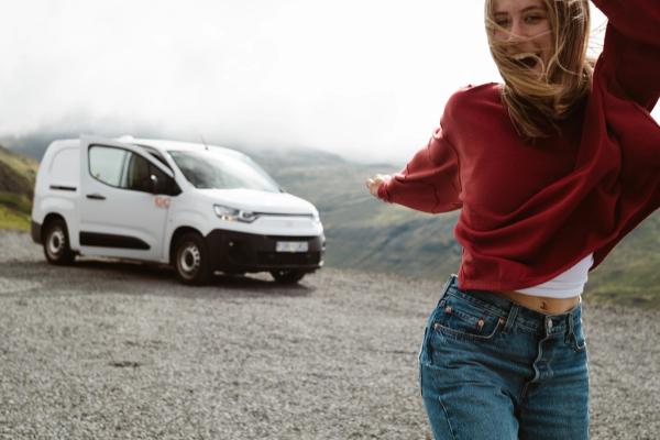 Happy woman jumping with arms outstretched in front of a white cargo van and mountains.