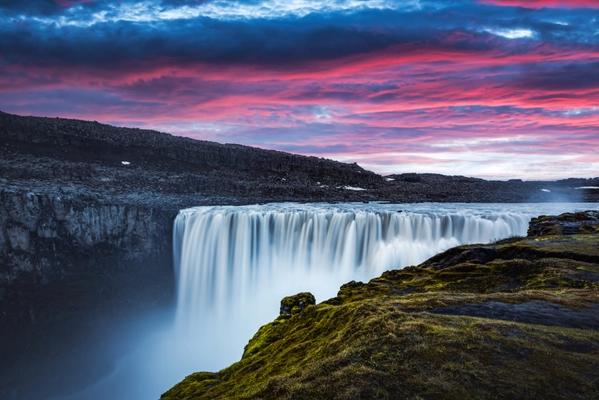 a waterfall with a sunset in the background and a cliff in the foreground at Dettifoss in iceland.