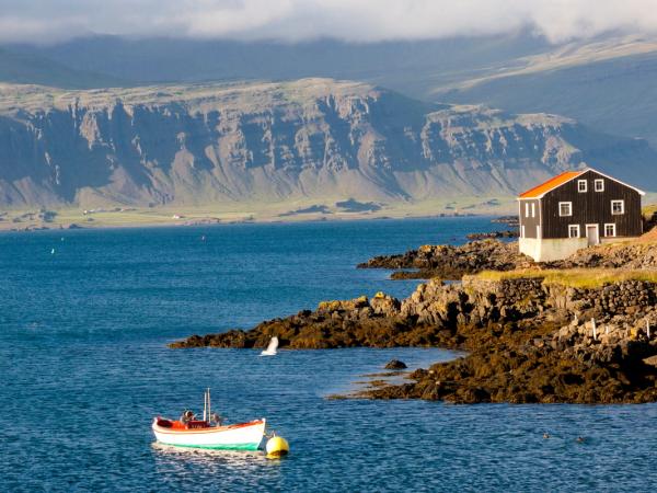 Casa marrón a lado del mar y un barco pequeño en el agua, Djúpivogur, Islandia
