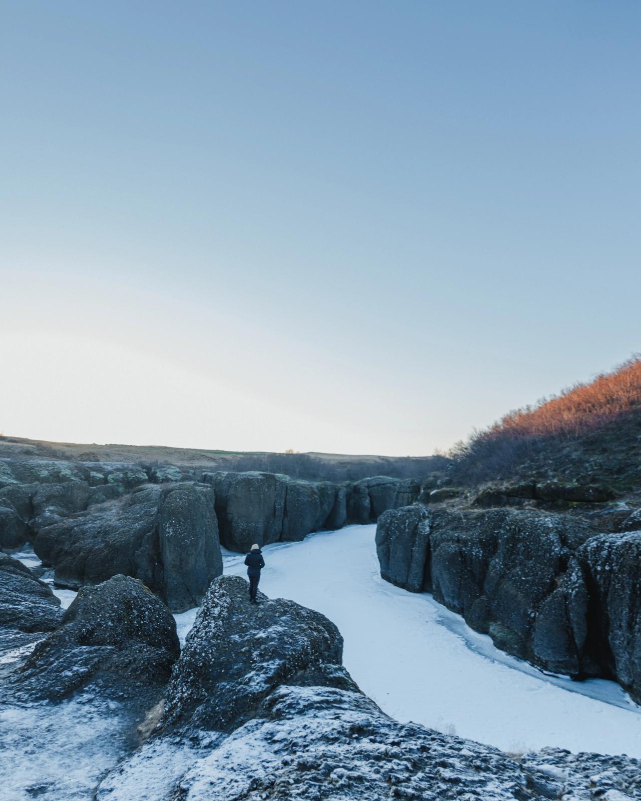 Una persona está parada sobre una roca cubierta de nieve, contemplando un cañón helado.
