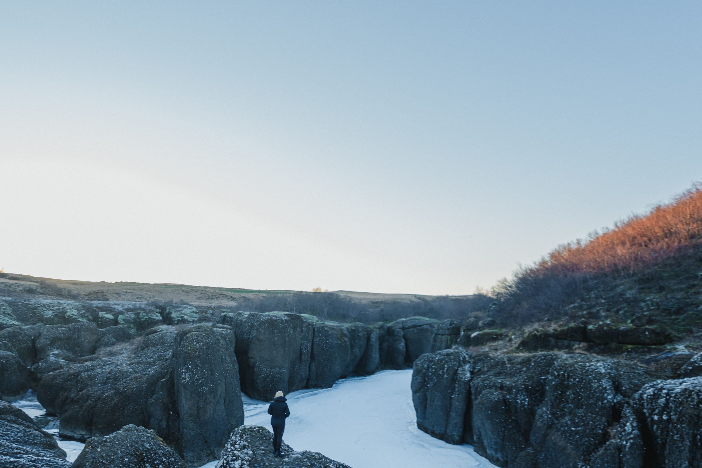 Una persona está parada sobre una roca cubierta de nieve, contemplando un cañón helado.