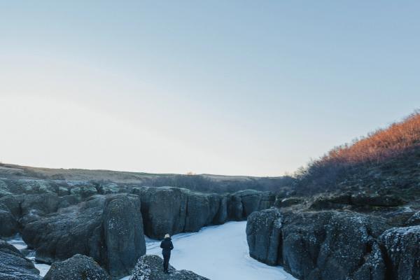 A person stands on a snow-dusted rock overlooking a frozen canyon.