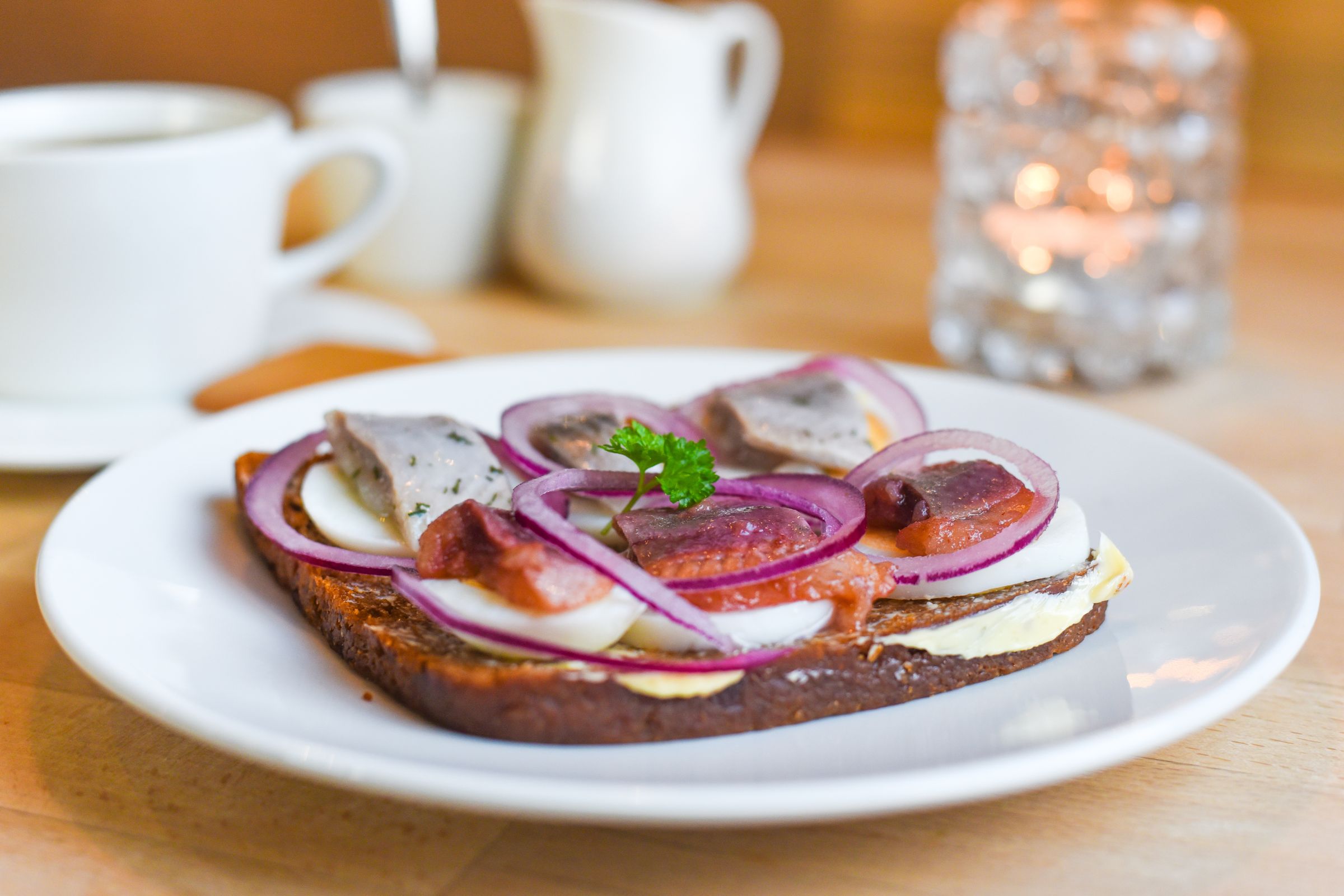 Un sándwich abierto de pan negro cubierto con lonchas de pescado, huevo duro, cebolla morada y perejil.