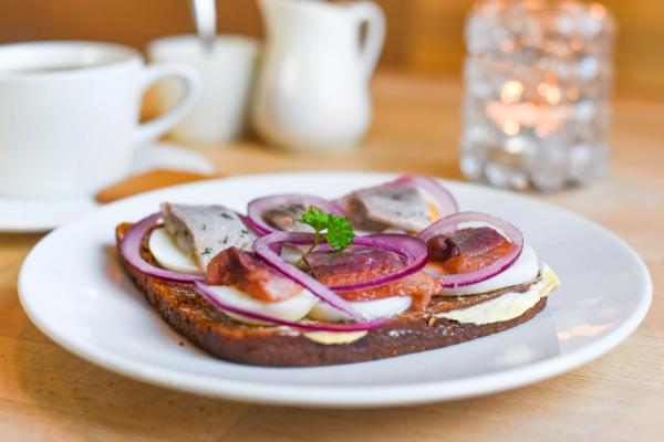 An open-faced sandwich on dark bread topped with fish slices, hard-boiled egg, red onion, and parsley.