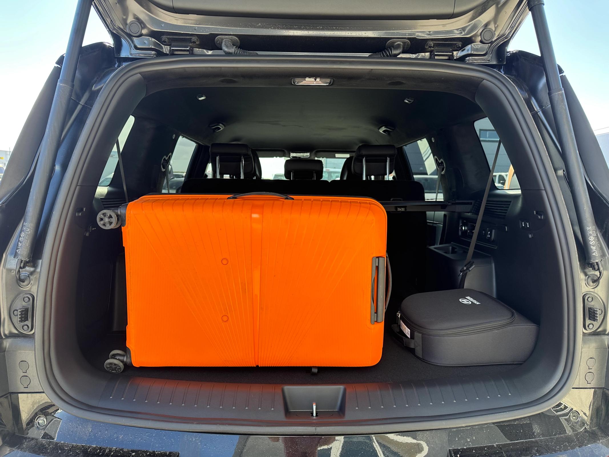 An open car trunk with a large orange suitcase and a black soft case.