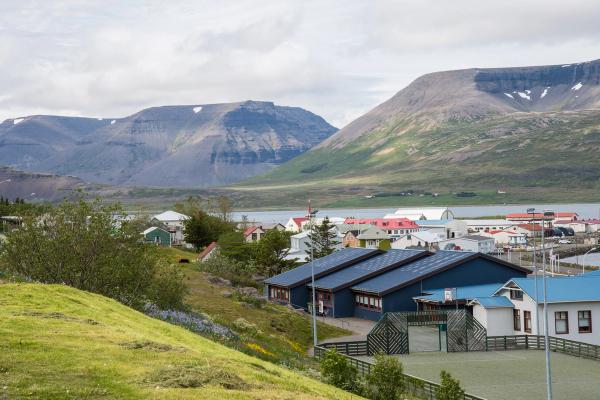 A village with colorful buildings by a fjord, backed by large mountains.