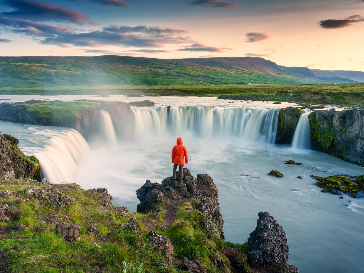 Hombre con una chaqueta roja subido a unas rocas mirando una cascada