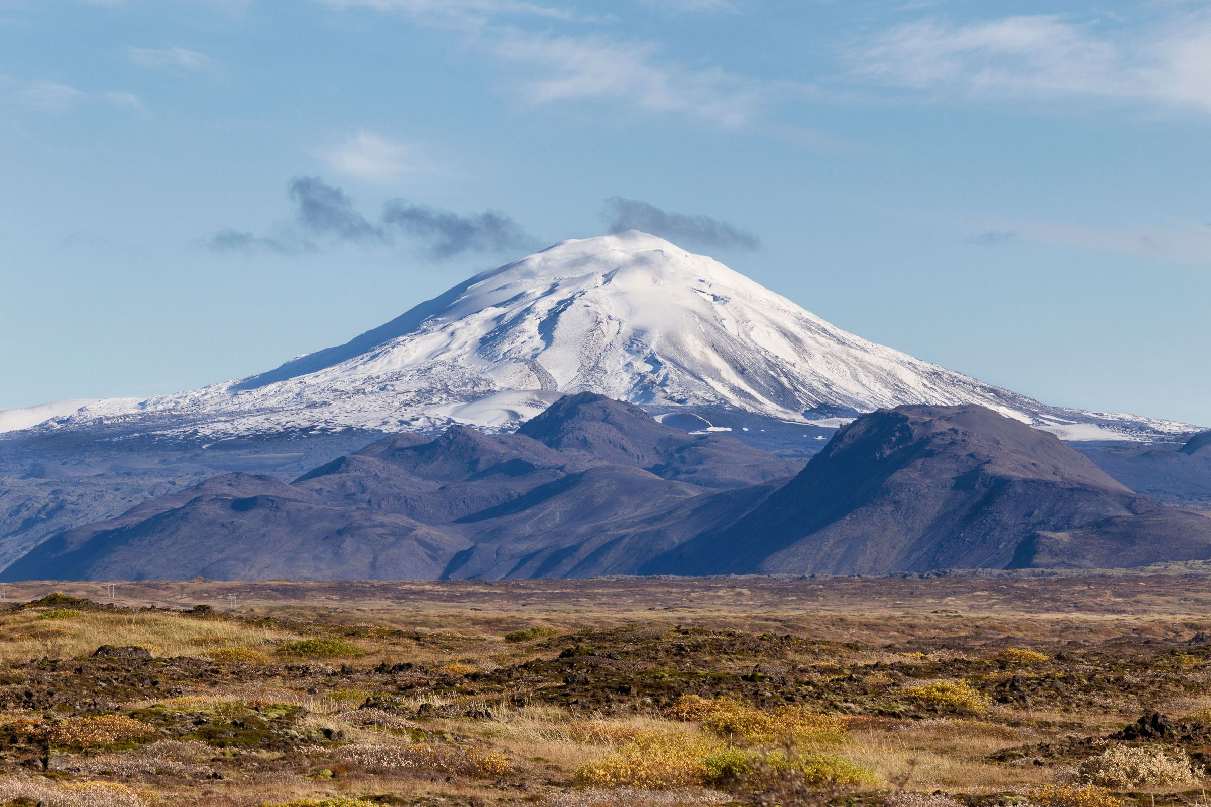 Hekla Volcano a mountain covered in snow is surrounded by mountains and a desert .