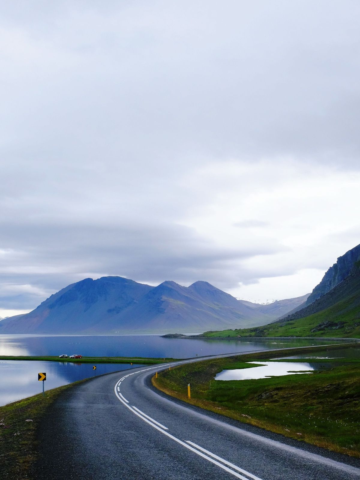 a road going through a mountainous area with a lake and mountains in the background .