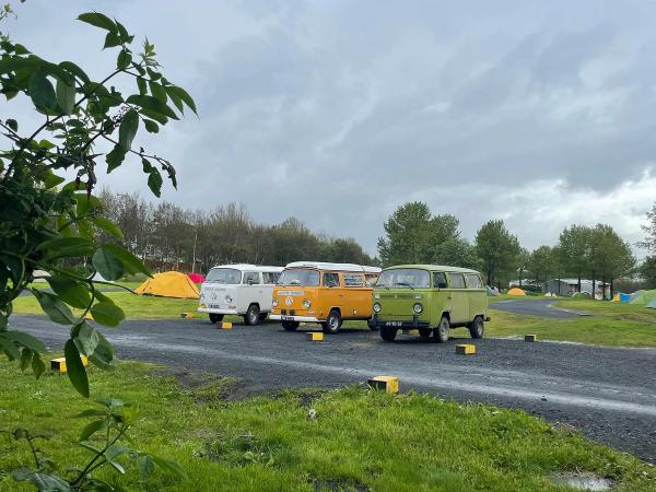 Tres campers en un camping con tiendas de campaña por detrás