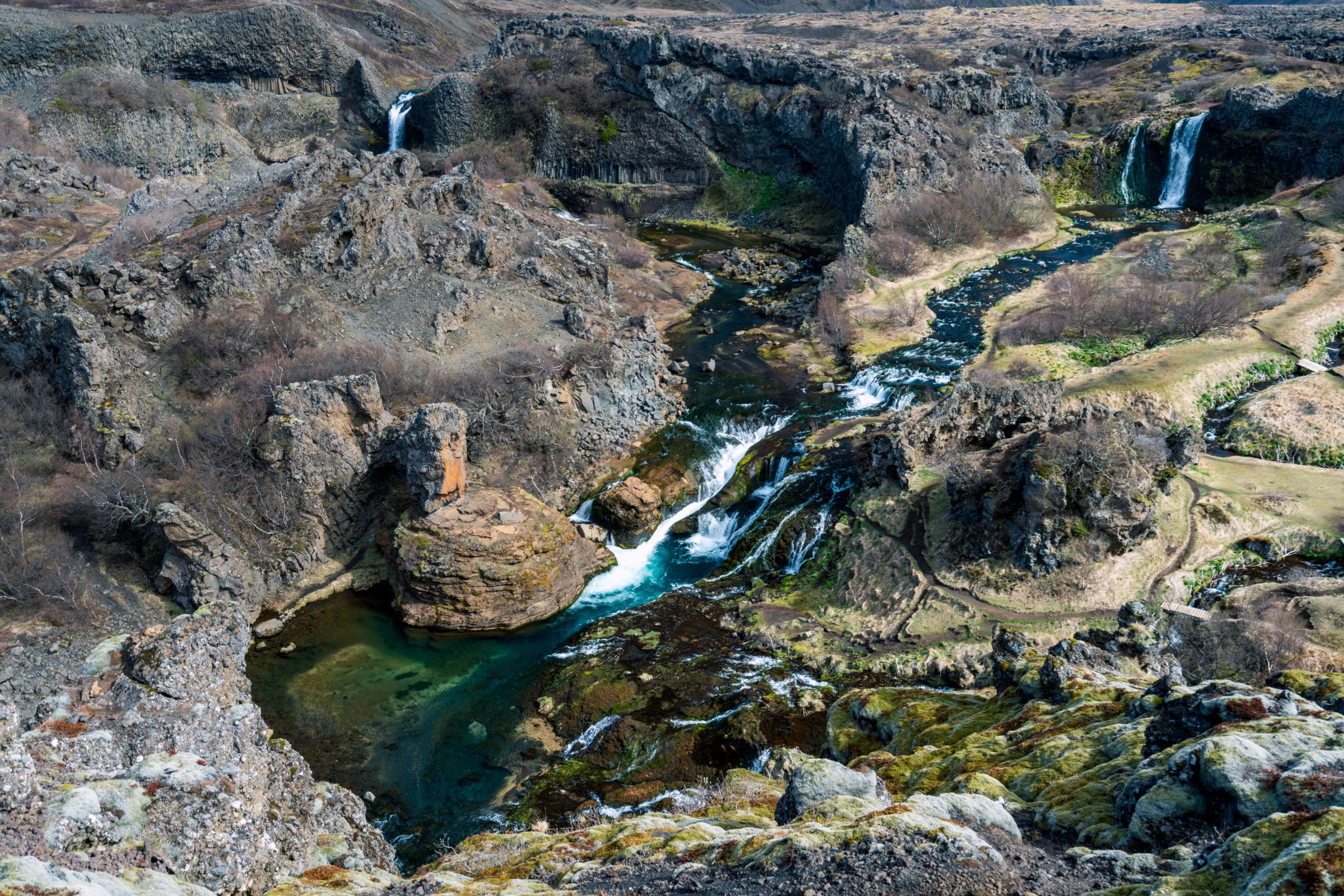 A rugged, rocky canyon with a winding river, several waterfalls, and bright turquoise pools.