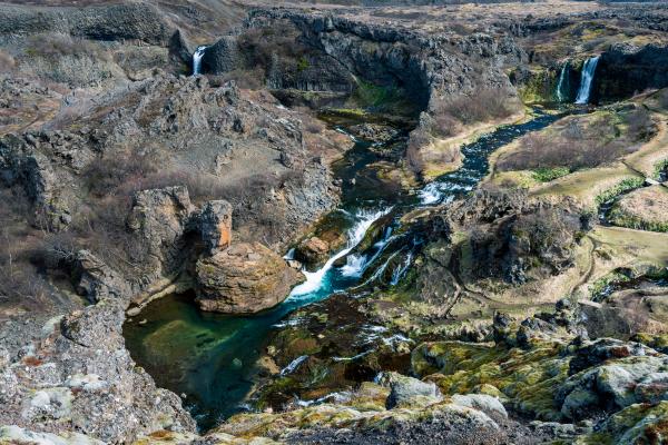 A rugged, rocky canyon with a winding river, several waterfalls, and bright turquoise pools.