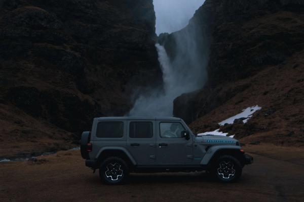 Jeep Wrangler rental car iceland A parked dark gray Jeep Wrangler Rubicon rental car near a stunning waterfall in iceland