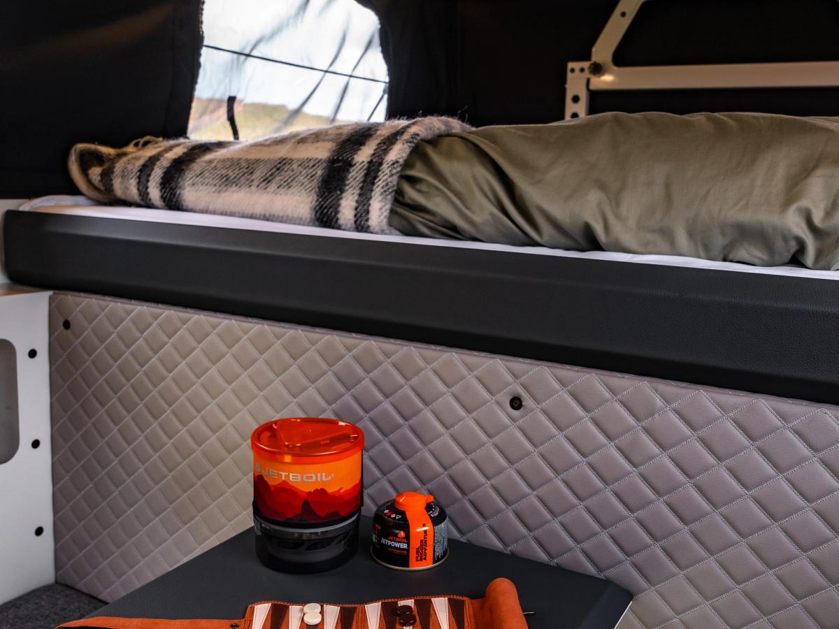 Detalles del juego de mesa Un juego de backgammon de viaje y una taza naranja sobre la mesa plegable situada debajo de la cama superior