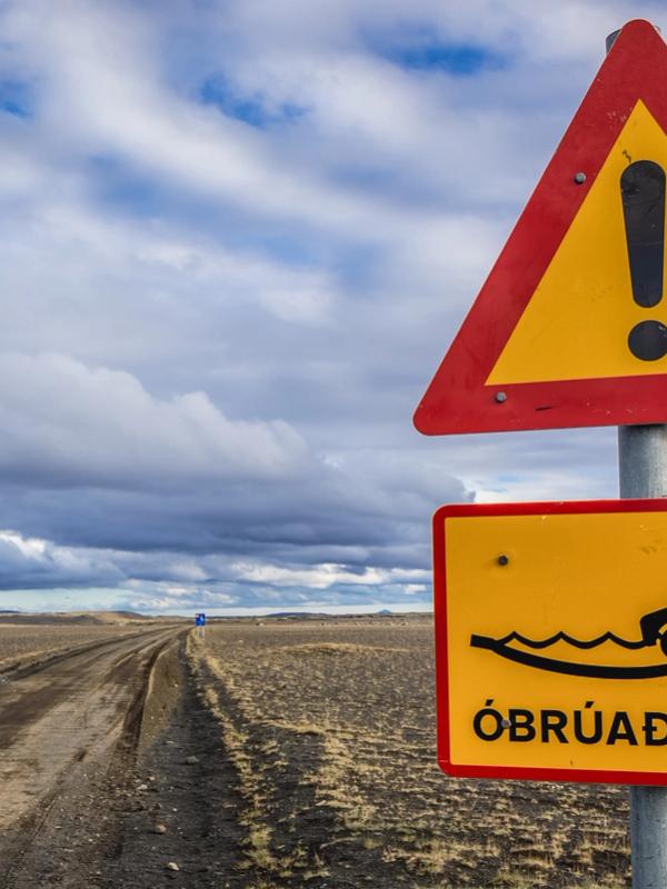 a yellow and red warning sign on a dirt road .