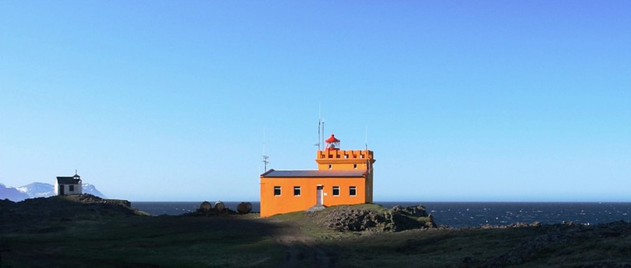 un bajo pero alto faro de color naranja con el mar de fondo en un día muy despejado