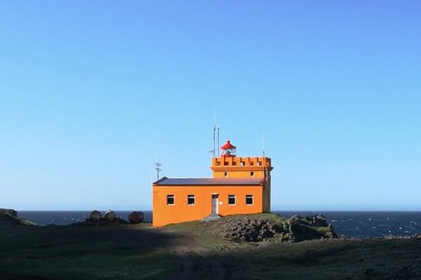 un bajo pero alto faro de color naranja con el mar de fondo en un día muy despejado