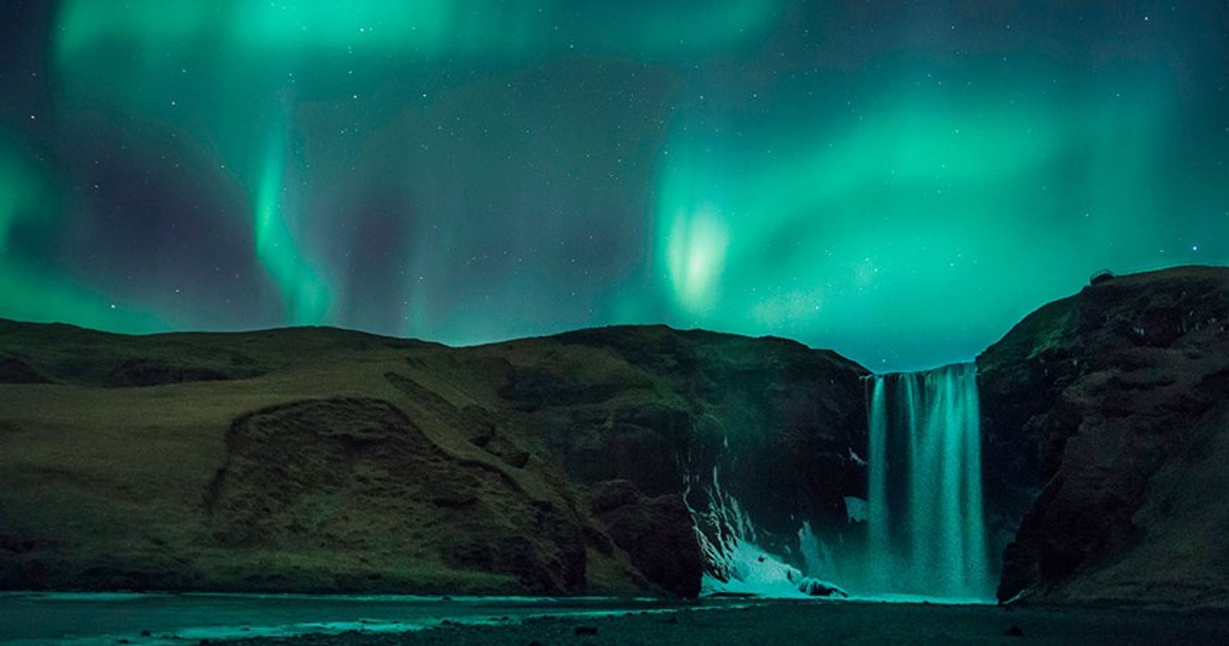 Las auroras boreales verdes iluminan una poderosa cascada en la noche.