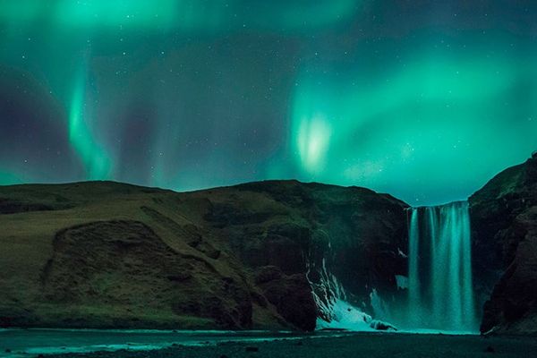 Las auroras boreales verdes iluminan una poderosa cascada en la noche.