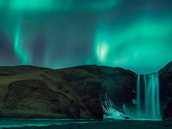 la aurora boreal brilla sobre una cascada en Islandia.