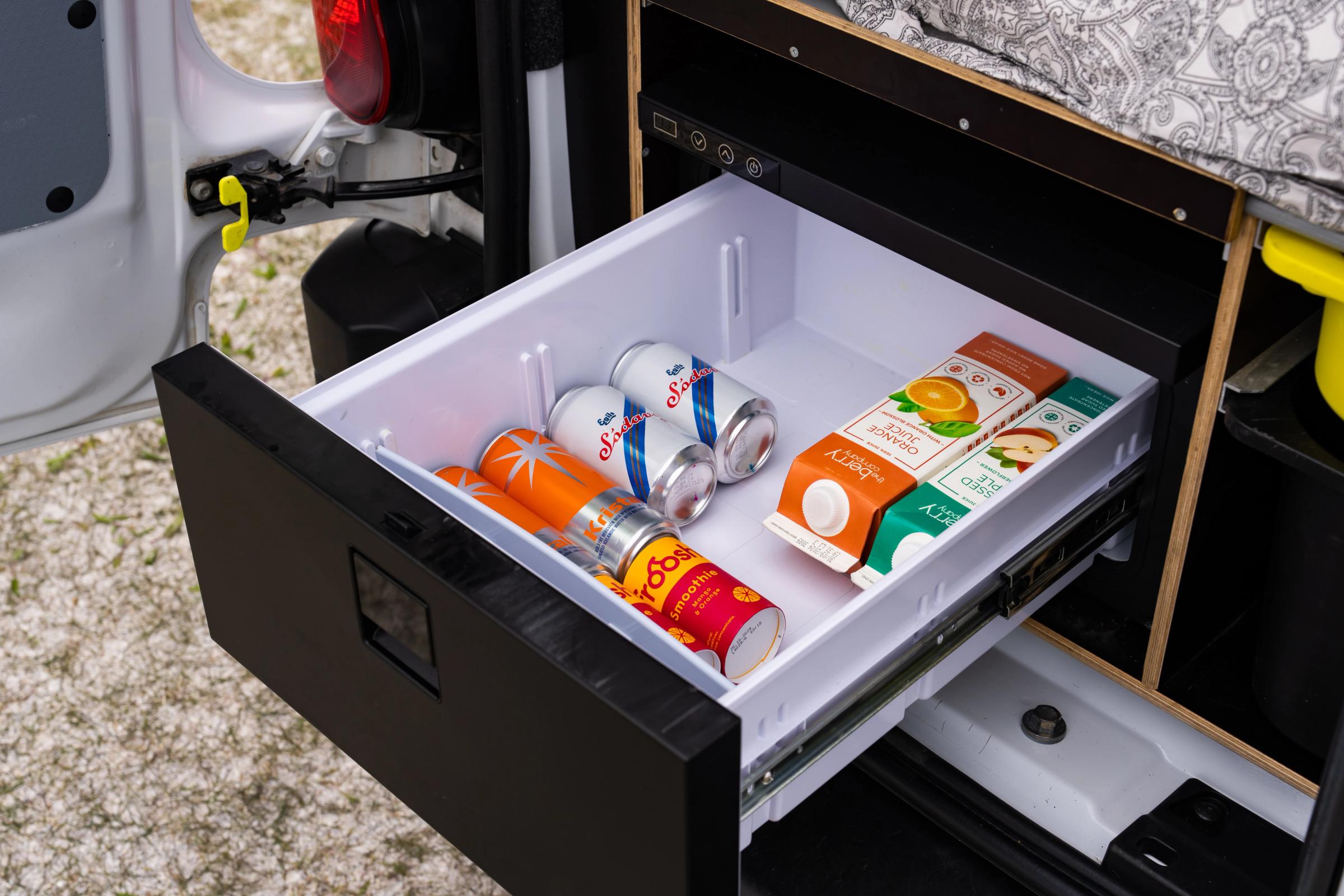 Cajón frigorífico extraíble abierto, con latas de bebidas y cartones de zumo bajo la plataforma de la cama