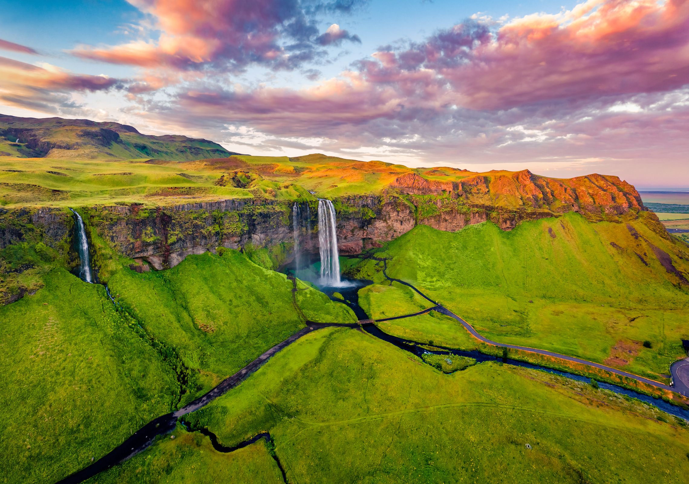 a waterfall falling from a moss covered cliff at dawn
