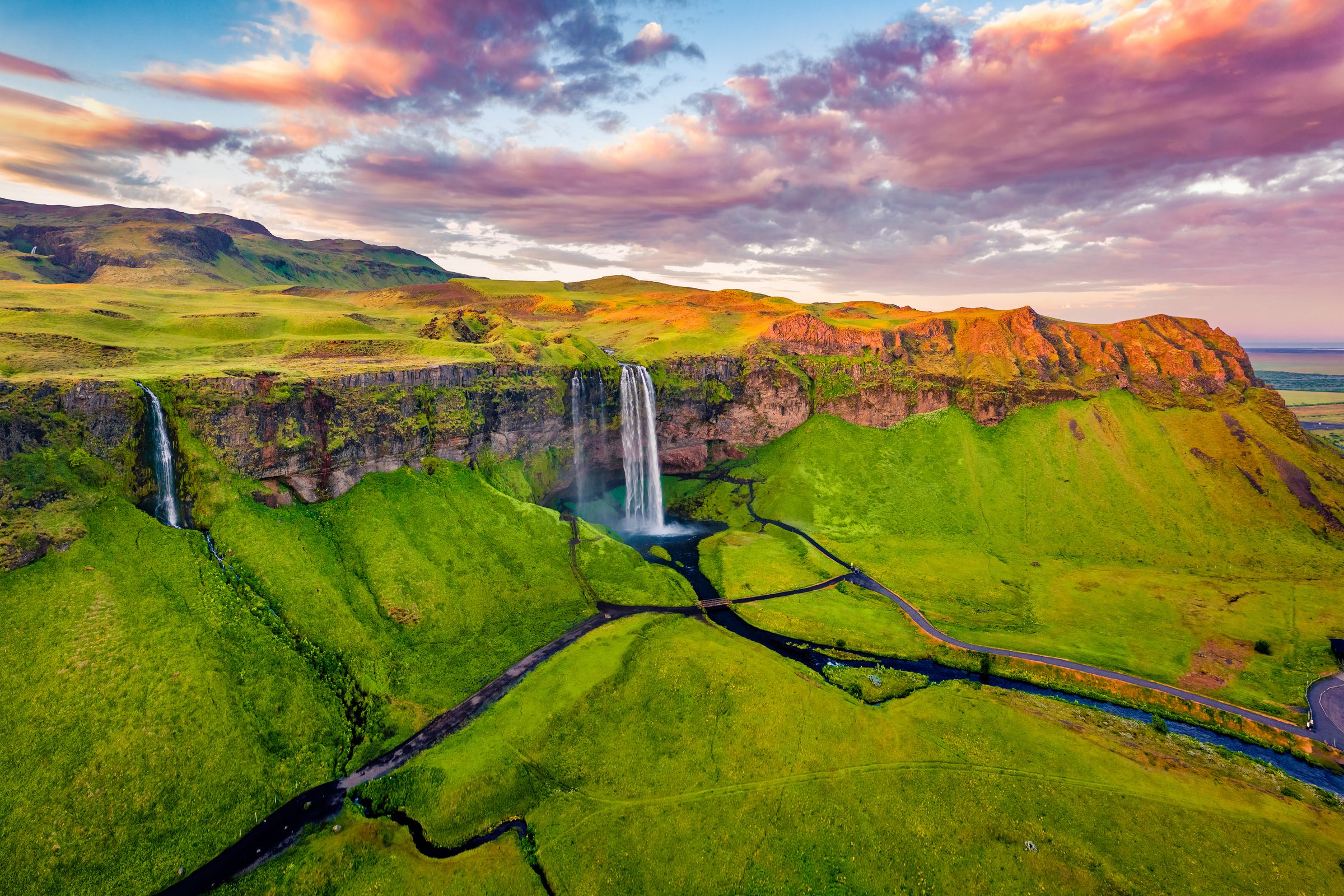a waterfall falling from a moss covered cliff at dawn