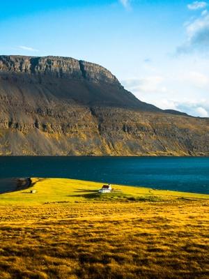 Casa en una pradera amarilla al lado del mar y una montaña detrás