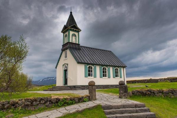 a small white church with a black roof and green shutters on a cloudy day .