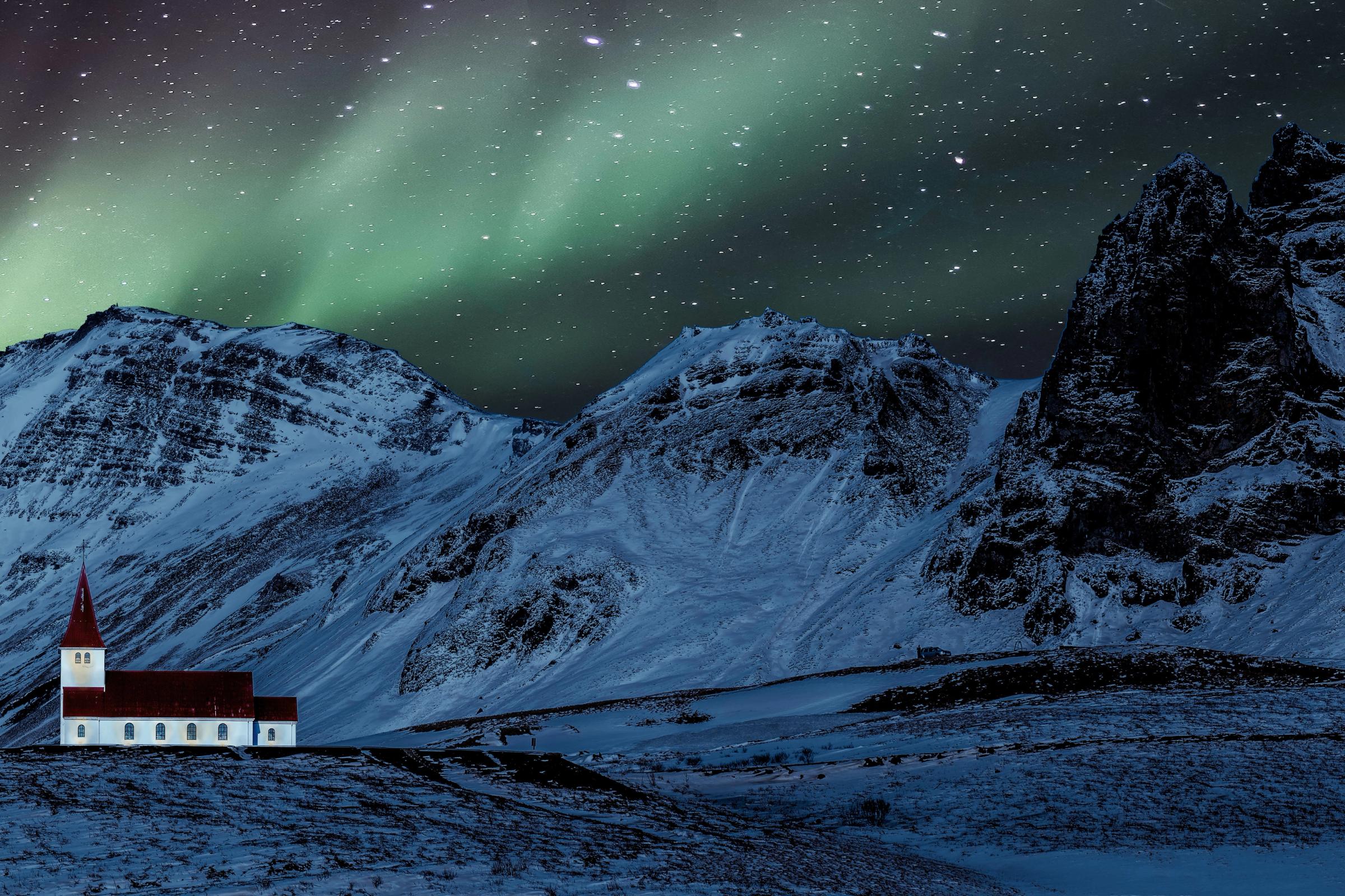 La Aurora Boreal bailando sobre una iglesia con montañas nevadas al fondo