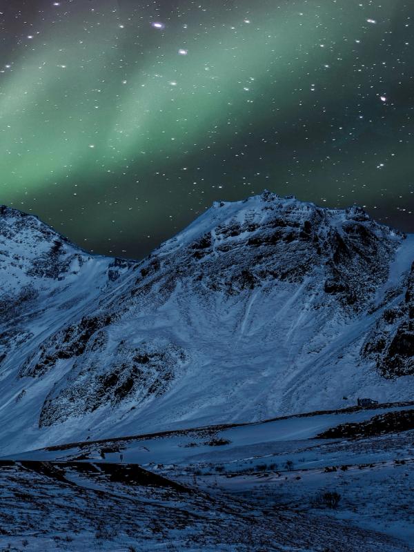 A white church with a red roof stands in a snowy mountain landscape under a starry sky with green aurora borealis.