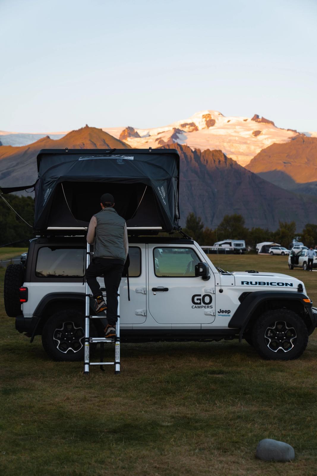 Hombre subiendo una escalera que lleva al techo de un Jeep blanco