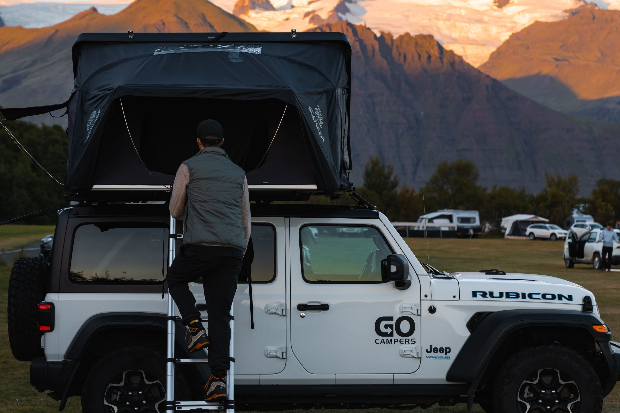 Hombre subiendo una escalera que lleva al techo de un Jeep blanco