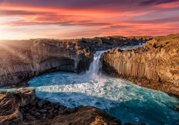 a waterfall in the middle of a canyon with a sunset in the background at Aldeyjarfoss in iceland.