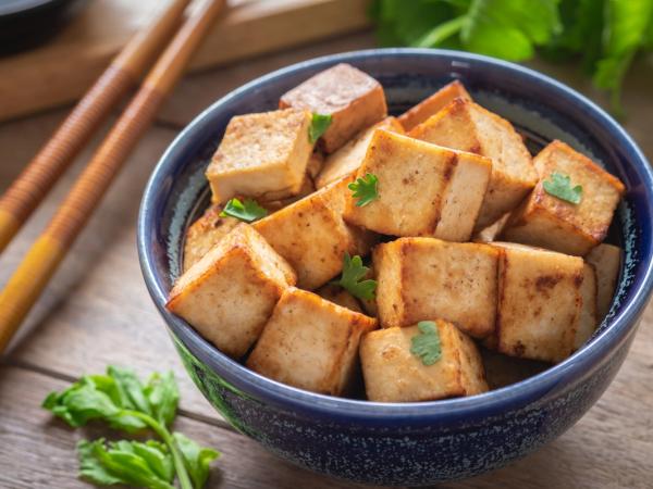 Golden-brown pan-fried tofu in a blue bowl with cilantro, next to chopsticks.
