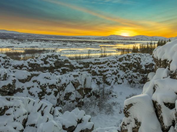 el sol se está poniendo sobre un paisaje nevado con montañas en el fondo .