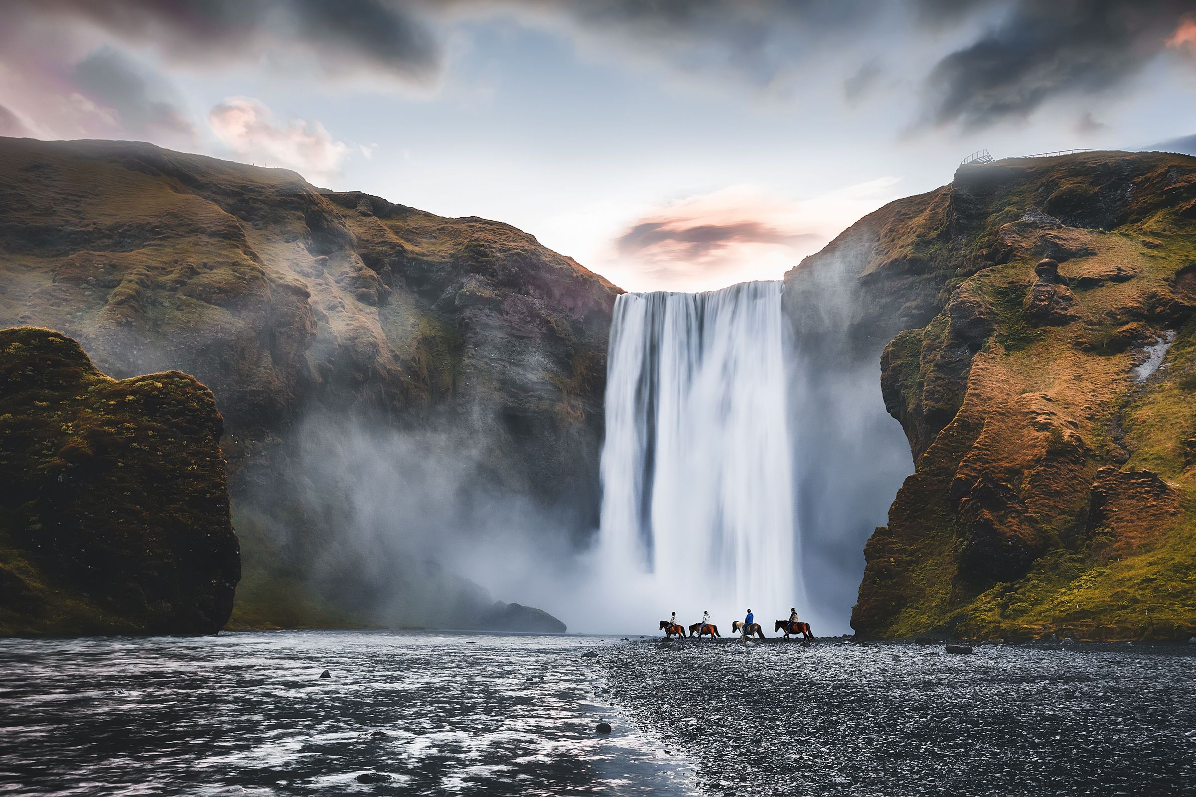 People horseback riding in front of a massive waterfall