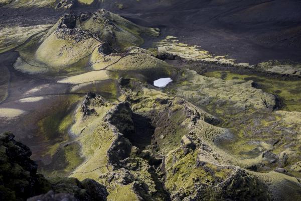Green mossy volcanic landscape with black sand and a small white pool.