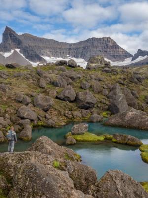 a man is standing on a rock near a lake in the mountains .