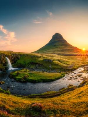 A vibrant sunset over Kirkjufell mountain, with Kirkjufellsfoss waterfall and a river in the foreground.