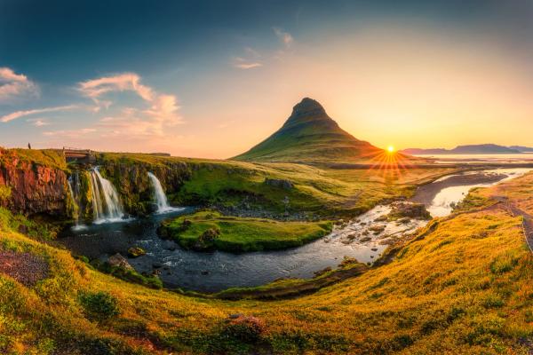 A conical mountain overlooks a multi-tiered waterfall and river in a golden sunset landscape.