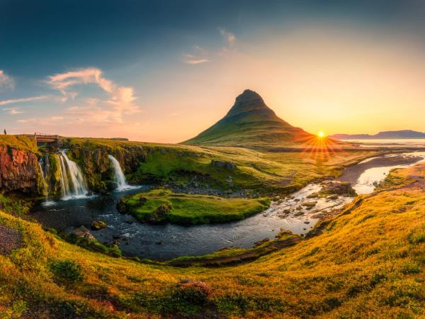 Kirkjufell mountain and Kirkjufellsfoss waterfall at sunset, with golden fields and a winding river.