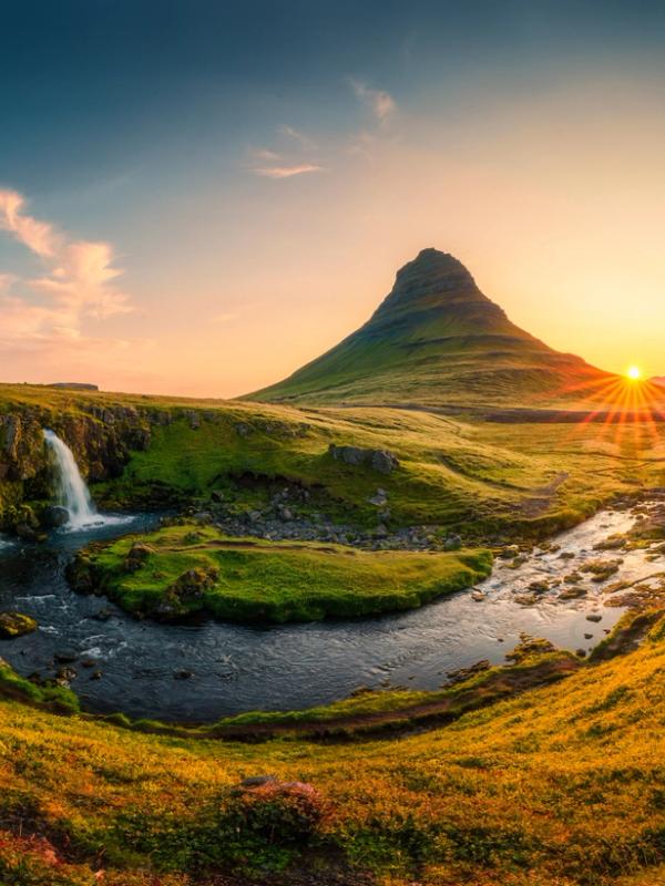A vibrant sunset over Kirkjufell mountain, with Kirkjufellsfoss waterfall and a river in the foreground.