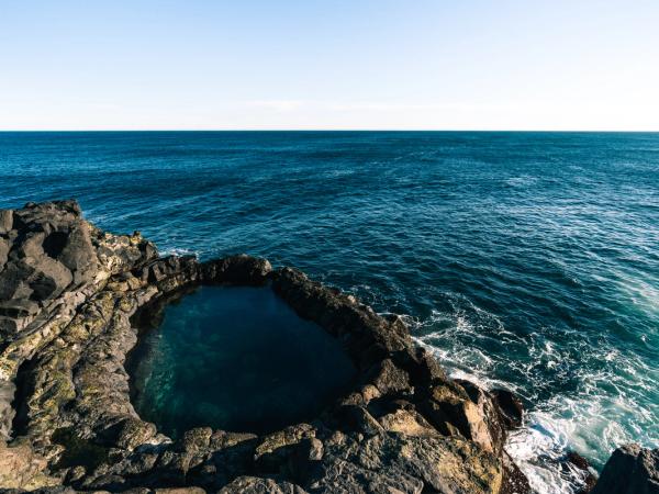 Natural rock pool in dark volcanic rock next to the deep blue ocean.