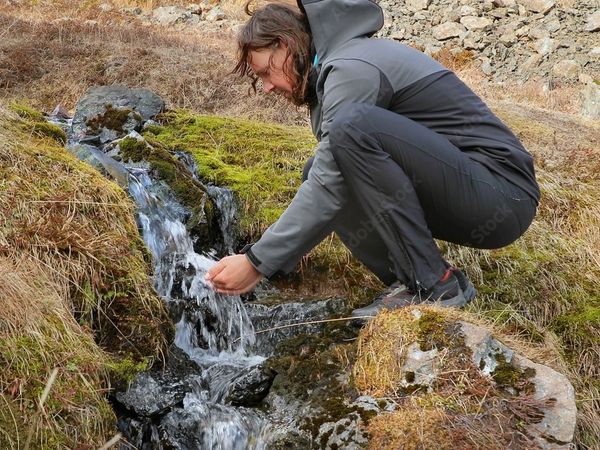 a woman is drinking water from a small stream .