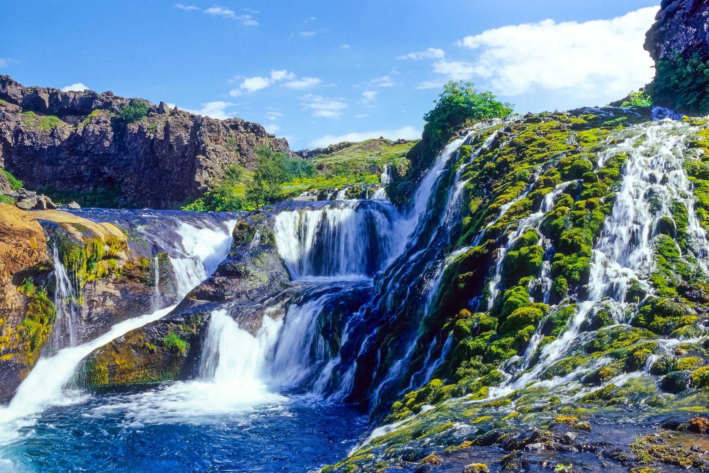 a waterfall is surrounded by rocks and moss on a sunny day .