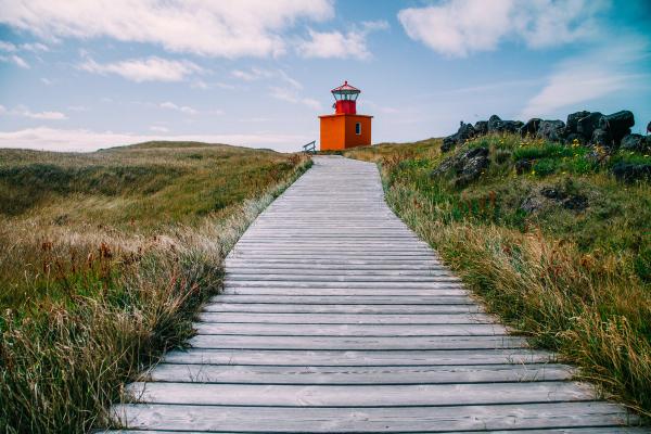 una pasarela de madera que conduce a un faro naranja en la cima de una colina.