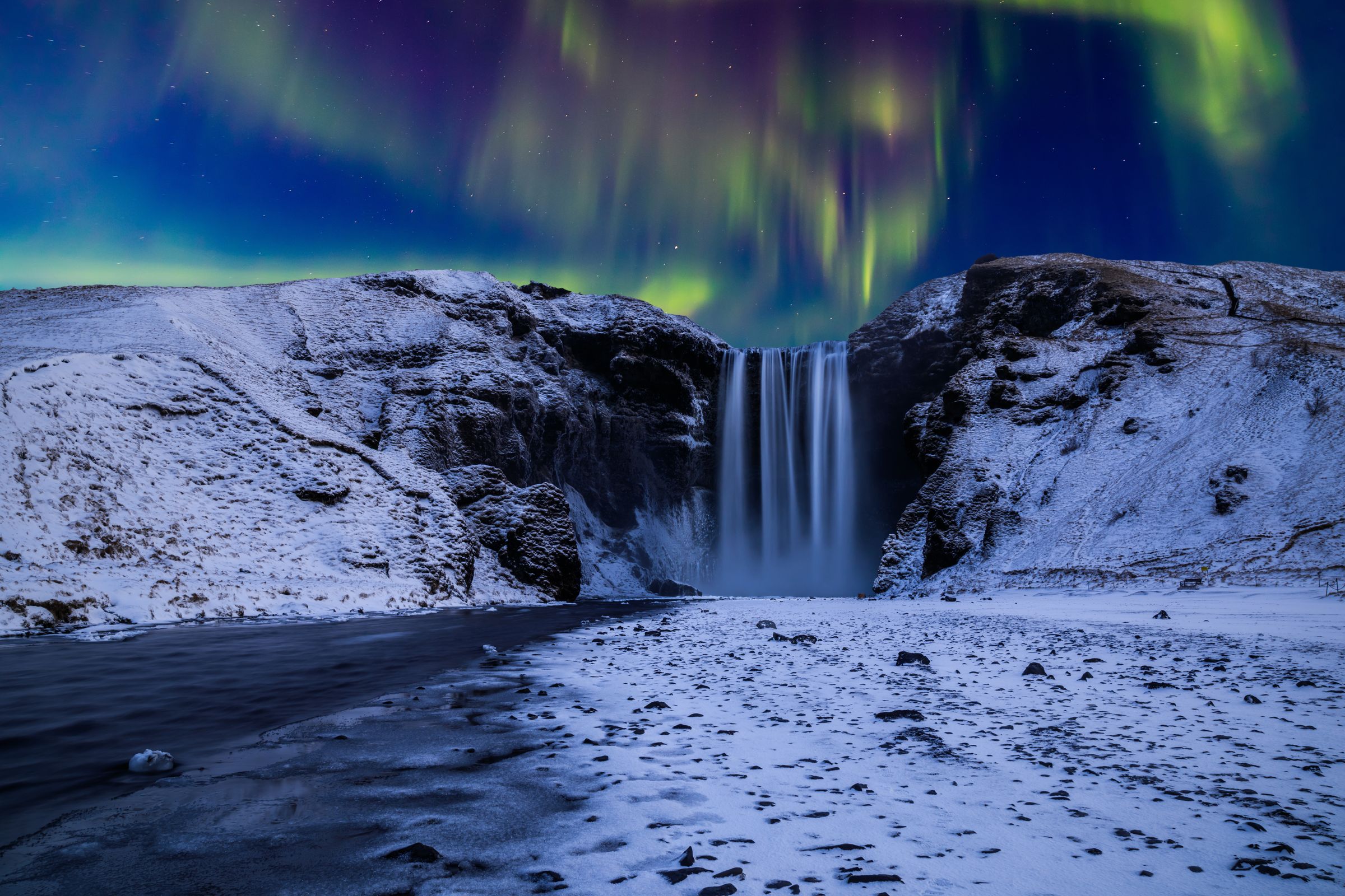 cascada rodeada de nieve durante la noche con la Aurora Boreal encima